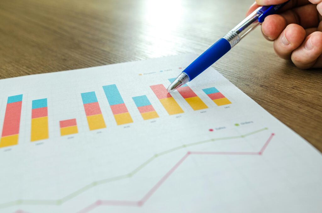 pexels-photo-590020-590020 Detailed close-up of a hand pointing at colorful charts with a blue pen on wooden surface.